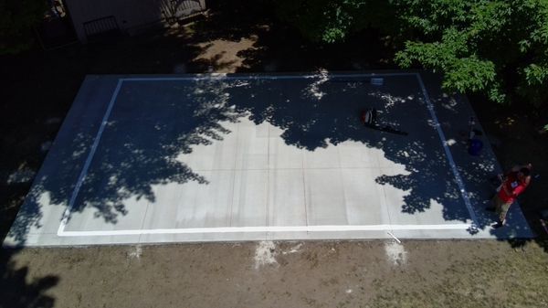 An aerial view of a concrete dance floor in a backyard surrounded by trees.