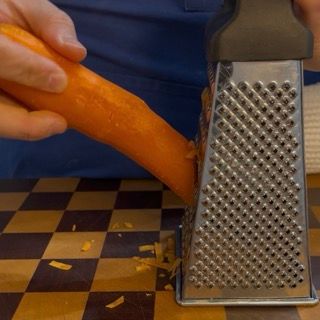 Utilizzo della grattugia a fori larghi per sminuzzare le carote pelate.