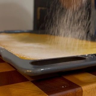 Una persona sta cospargendo zucchero a velo su un tagliere.