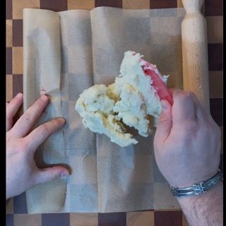 Una persona tiene in mano un pezzo di pasta su un foglio di carta da forno