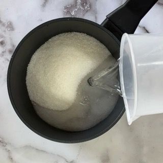 Una tazza graduata viene versata in una pentola di zucchero.