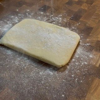 Un pezzo di pasta è appoggiato su un tagliere di legno ricoperto di farina