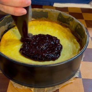Una persona sta spalmando la gelatina su una cheesecake in una teglia