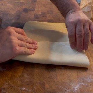 Una persona sta piegando un pezzo di pasta su un tavolo di legno.
