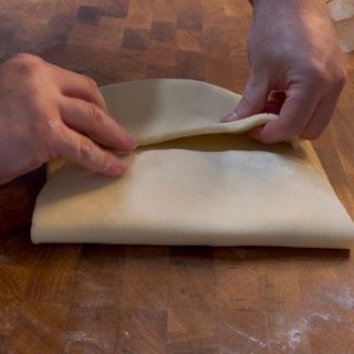 Una persona sta piegando un pezzo di pasta su un tavolo di legno