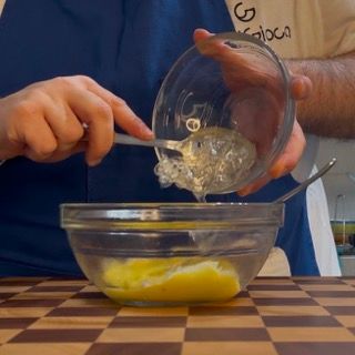 Una persona che versa del liquido in una ciotola di vetro con un cucchiaio