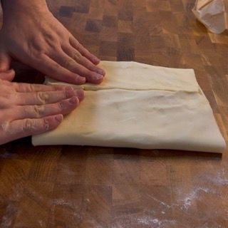 Una persona sta piegando un pezzo di pasta su un tavolo di legno