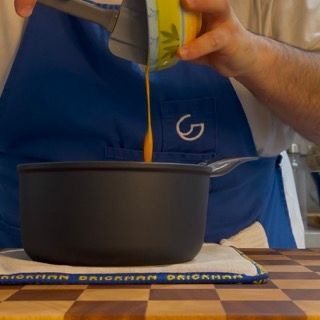 Una persona che versa del liquido in una pentola su cui è scritta la lettera g