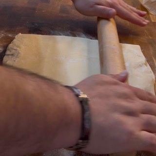Una persona sta stendendo la pasta con un mattarello su un tavolo di legno.