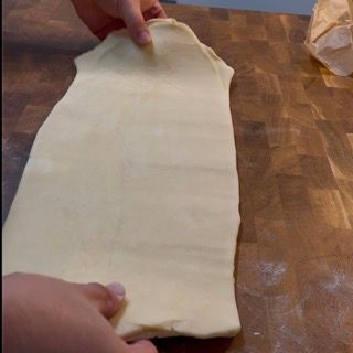 Una persona tiene in mano un pezzo di pasta su un tavolo di legno.