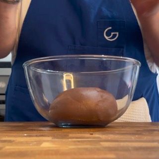 Una persona con un grembiule blu tiene in mano una ciotola di vetro piena di pasta