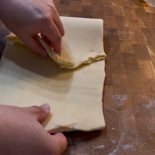 Una persona sta piegando un pezzo di pasta su un tagliere