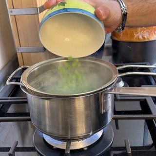 Aggiunta dei piselli nella pentola per la cottura delle verdure.