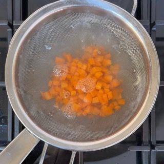 Cubetti di patate e carote tuffati in acqua bollente.