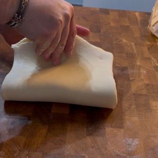 Una persona sta stendendo un pezzo di pasta su un tagliere di legno.