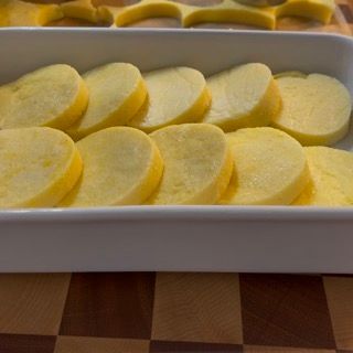 Un contenitore bianco pieno di patate a fette su un tavolo a scacchi