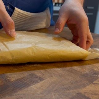 Una persona tiene in mano un pezzo di carta oleata su un tavolo di legno