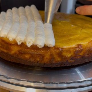 Una persona sta glassando una cheesecake con panna montata