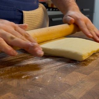 Una persona sta stendendo un pezzo di pasta con un mattarello
