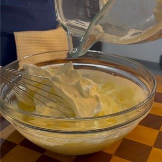 La panna montata viene versata in una ciotola di vetro con una frusta.