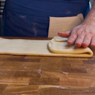 Una persona sta piegando un pezzo di pasta su un tavolo di legno