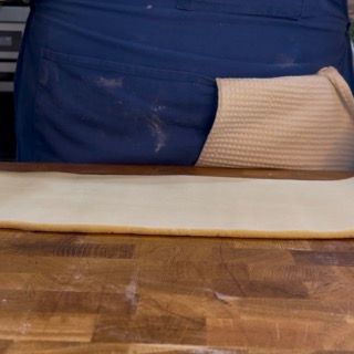 Una persona sta stendendo la pasta su un tagliere di legno.