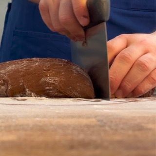 Una persona sta tagliando una pagnotta di pane su un tagliere
