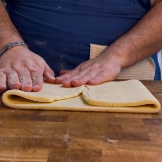 Una persona sta piegando un pezzo di pasta su un tavolo di legno