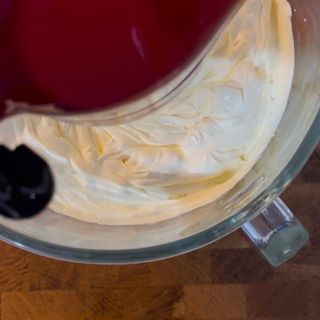 Una persona sta versando un liquido rosso in una ciotola di panna montata.