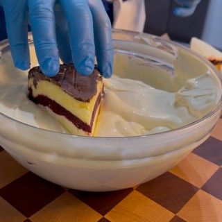 Una persona che indossa guanti blu tiene in mano un pezzo di torta in una ciotola di panna montata.