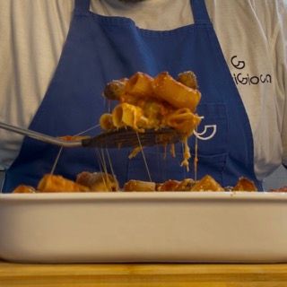 Una persona che indossa un grembiule blu tiene una forchetta sopra una casseruola di pasta