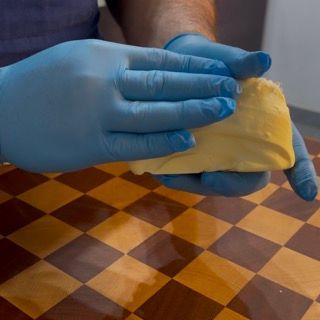 Una persona che indossa guanti blu tiene in mano un pezzo di burro