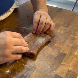 Una persona sta impastando un pezzo di pasta su un tavolo di legno.