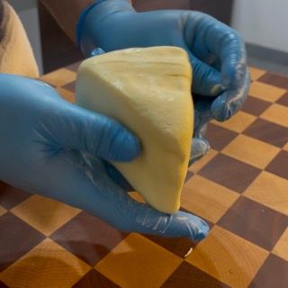Una persona che indossa guanti blu tiene in mano un pezzo di formaggio