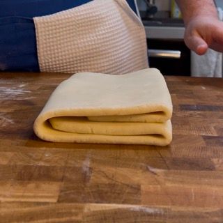 Una persona sta piegando un pezzo di pasta su un tavolo di legno