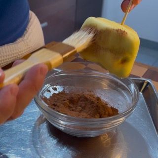 Una persona tiene un pennello sopra una ciotola di cacao in polvere