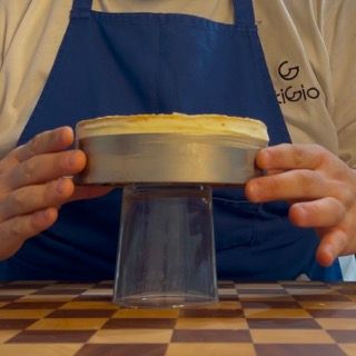 Una persona che indossa un grembiule blu tiene una torta in cima a un bicchiere