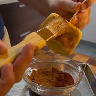 Una persona tiene un pennello sopra una ciotola di polvere marrone