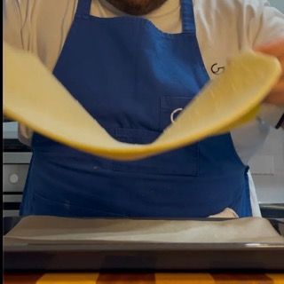 Un uomo con un grembiule blu sta lanciando un pezzo di pasta