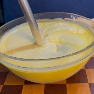 Una ciotola di liquido giallo con un cucchiaio dentro su un tavolo a scacchi.