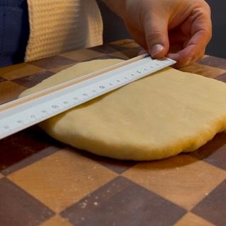 Una persona sta misurando un pezzo di pasta con un righello