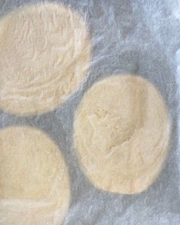 Tre cerchi di pasta sono appoggiati su un pezzo di carta oleata.