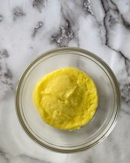 Una ciotola di vetro piena di liquido giallo su una superficie di marmo.