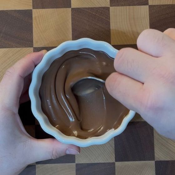 Una persona tiene in mano una ciotola di budino al cioccolato con un cucchiaio dentro