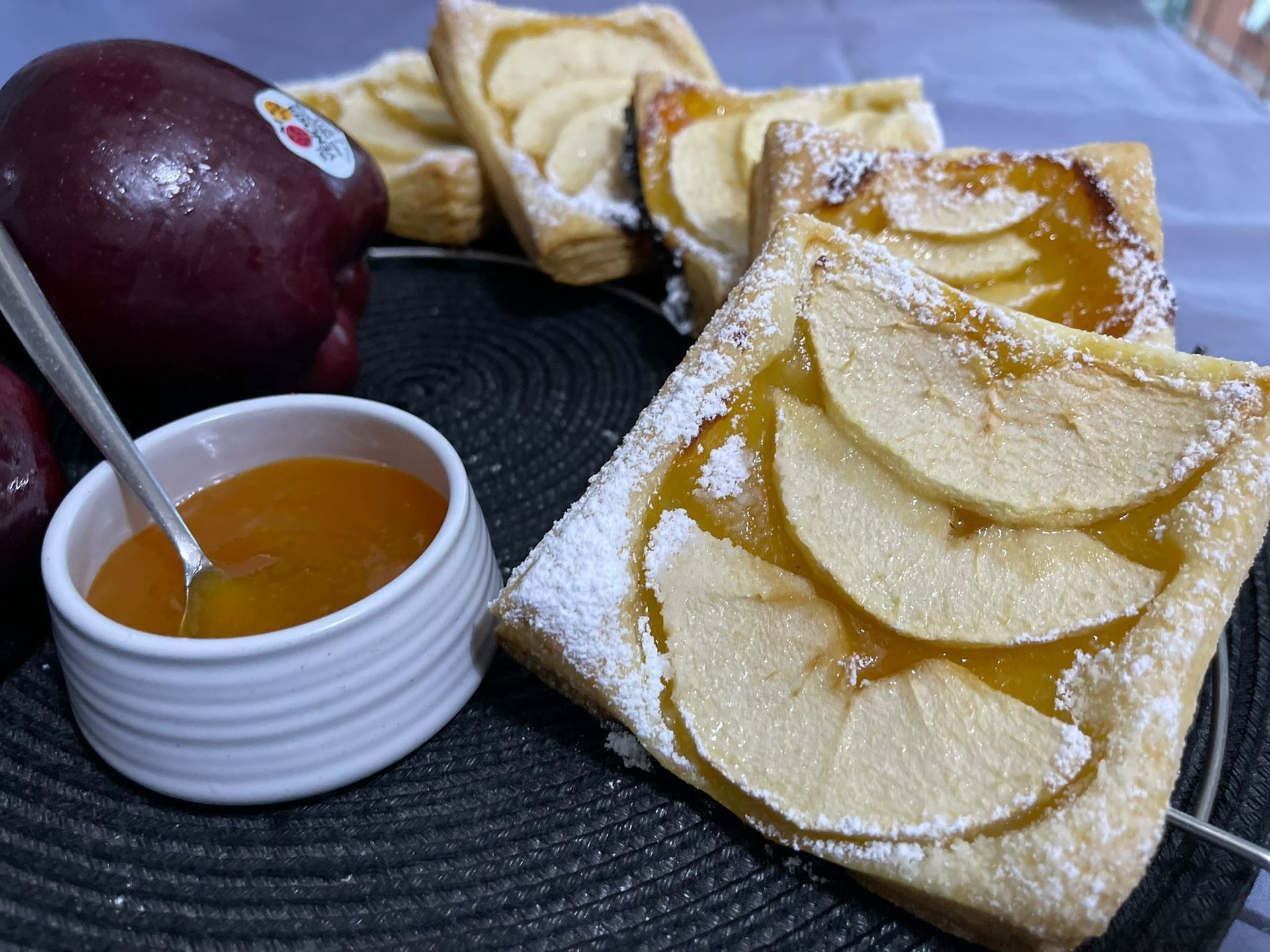 Un primo piano di un dolce con mele e una ciotola di marmellata su un tavolo.
