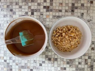 Una ciotola di salsa al cioccolato accanto a una ciotola di noci tritate.