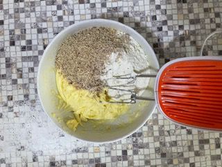 Una ciotola di pastella con noci e farina accanto a un mixer.