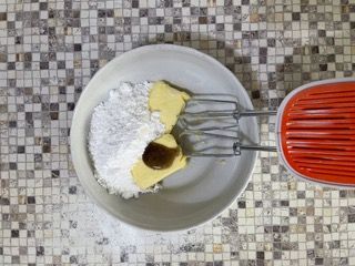 Una ciotola con zucchero a velo, burro e vaniglia accanto a un mixer.