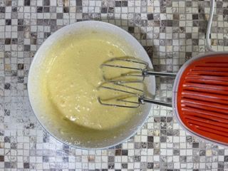 Una ciotola di pastella accanto a un mixer su un tavolo piastrellato.