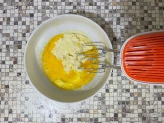 Una ciotola di uova e burro accanto a un mixer su un bancone piastrellato.